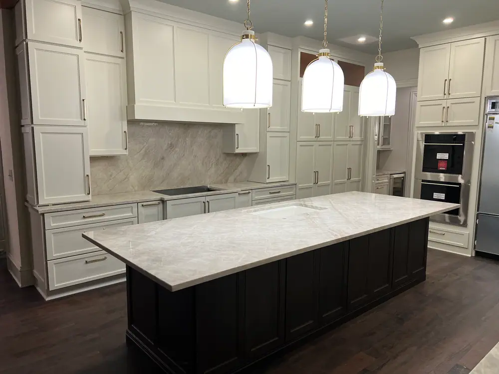 Finished kitchen with a veined stone island and a full-height slab backsplash under pendant lights