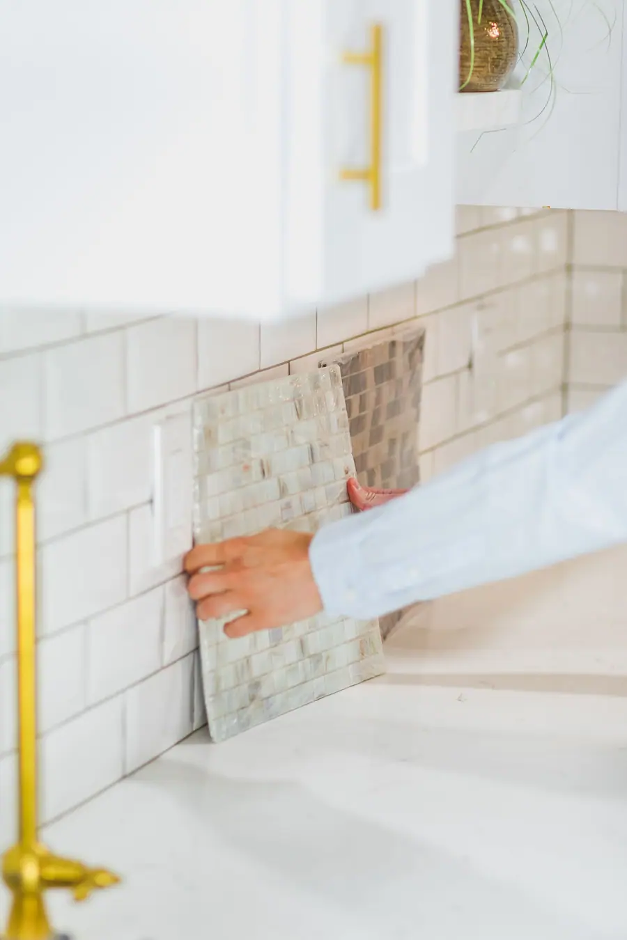 A sheet of marble mosaic tile being pressed onto a kitchen backsplash